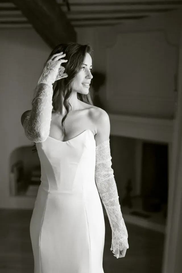 La mariée debout dans sa robe en crêpe et manches de dentelle