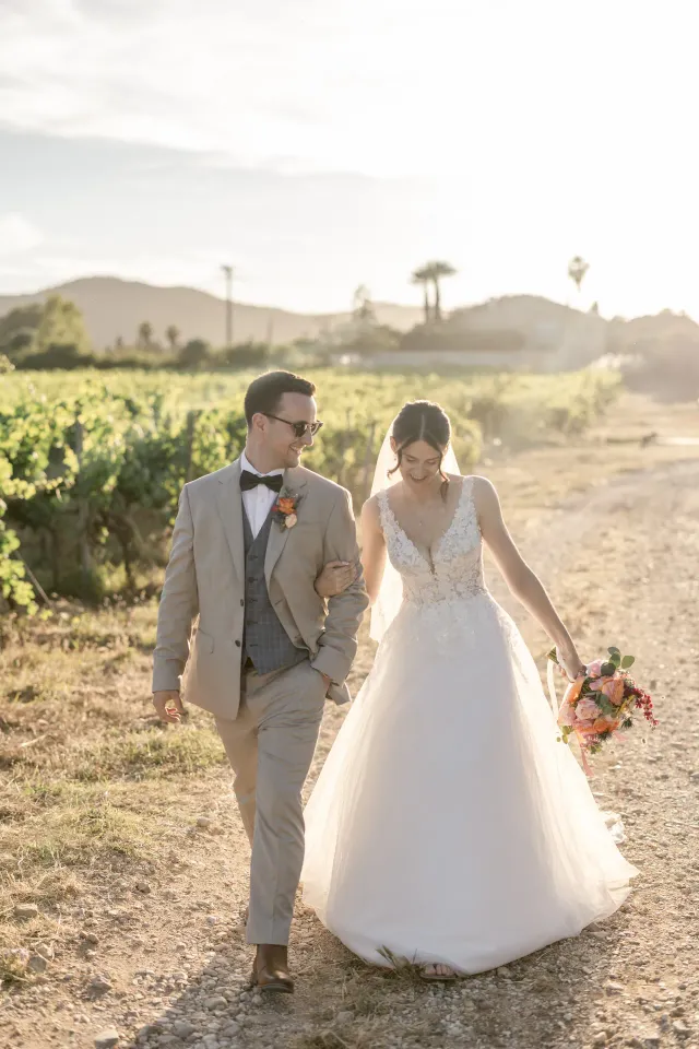 The couple walking through the estate's vines in golden light