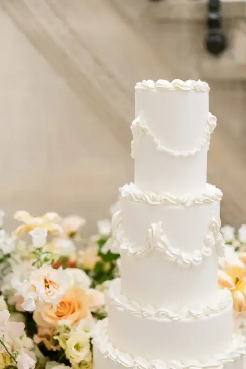 White tiered wedding cake surrounded by pastel flowers