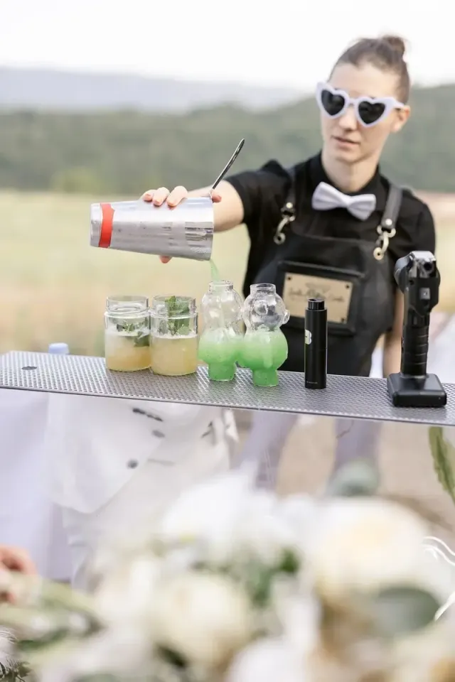Bartender pouring green cocktails in front of the hills, wedding cocktail bar