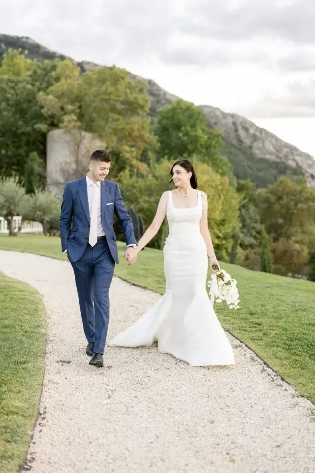 Bride and groom walking hand in hand on a gravel path facing the mountains
